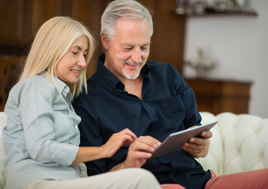 An older couple sitting together on a sofa, looking at a tablet