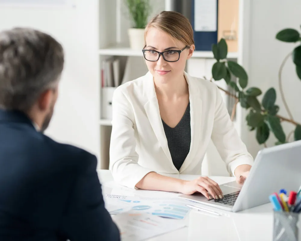 A consultant at her desk listening to a client across the table